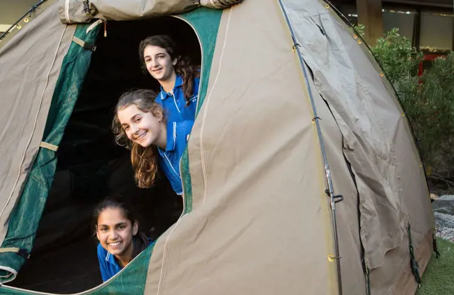 Three students poking heads out of Zoosnooz tents smiling during overnight program