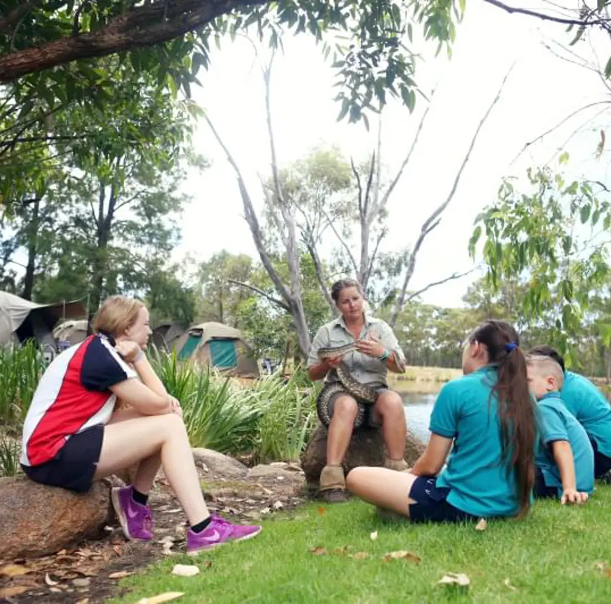 A small group of students with Taronga educator sitting on rocks in outside learning space at Taronga Western Plains Zoo