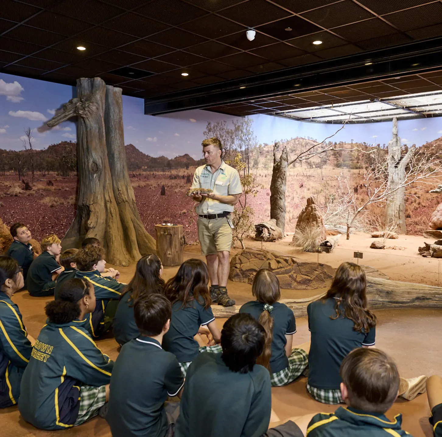 Students seated indoors listening to a guide in a desert-themed immersive classroom.