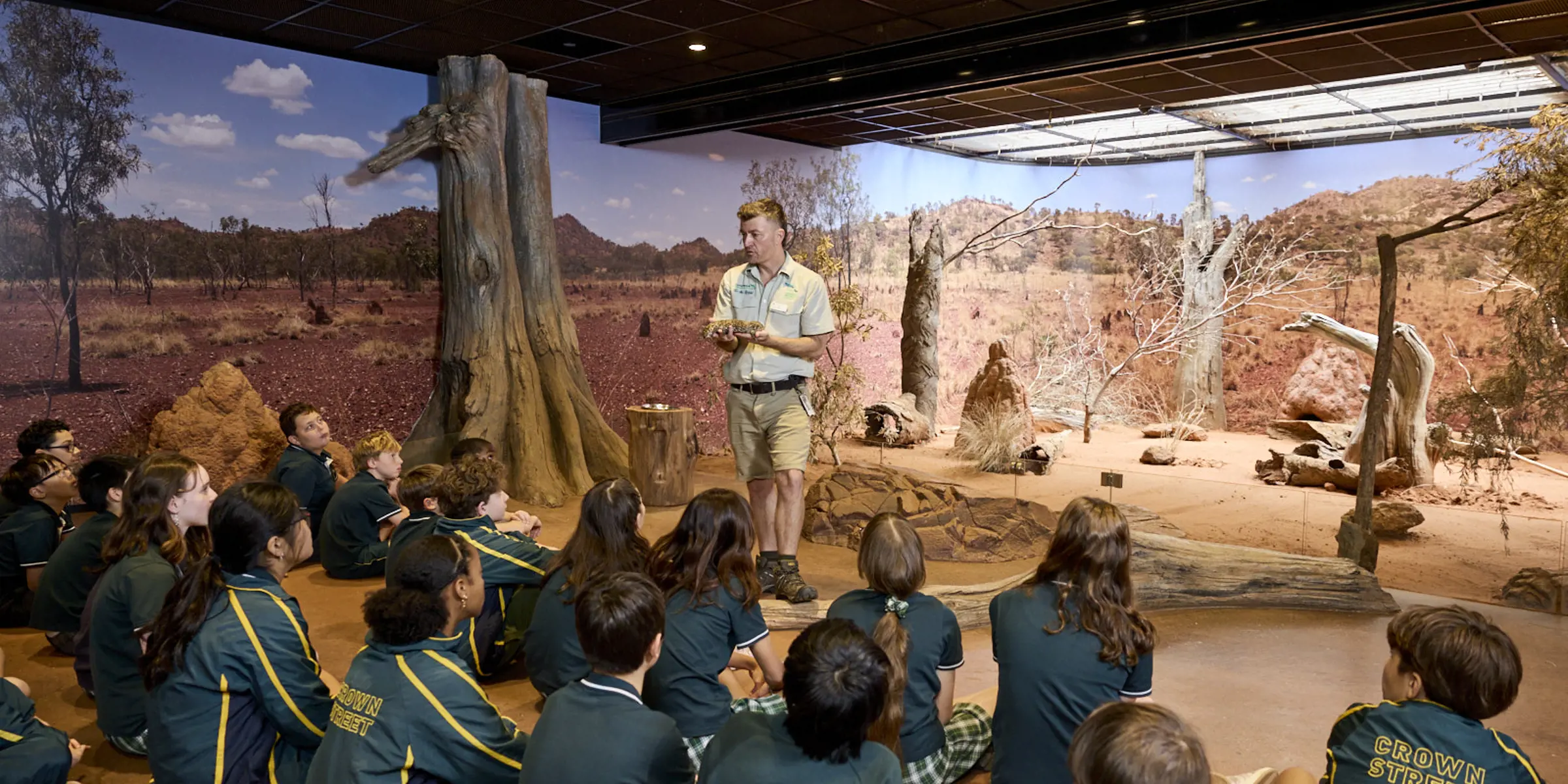 Students seated indoors listening to a guide in a desert-themed immersive classroom.