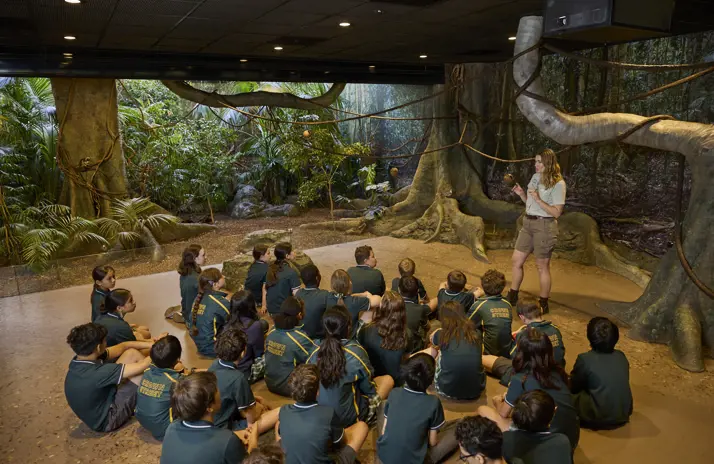 Students seated indoors listening to a teacher in a rainforest-themed immersive classroom.