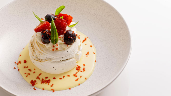 Wattleseed pavlova with passionfruit curd, whipped cream and berries.